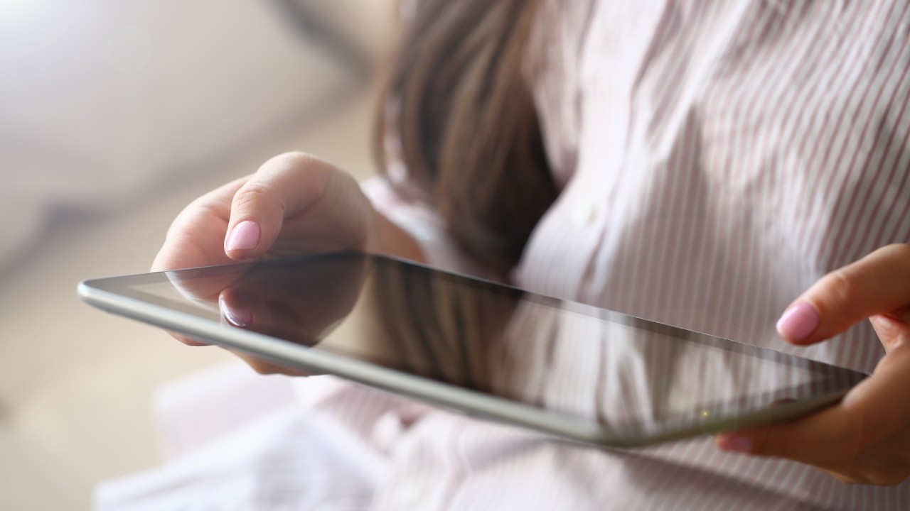 Female hand holds black tablet pad in home setting while sitting on couch engaged an internet surfing using application mail tracking food delivery display leisure listering music concept closeup.